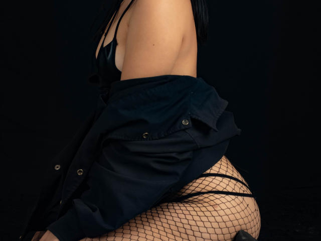YanNyan with black fishnet stockings, a black bra, and an unbuttoned dark shirt, showing her bare ass and a side of her tits. Dark background.