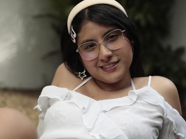 TereCarpert with glasses, white ruffled top, star earrings, and beige headband, smiling at camera, showing small tits, brown skin, and black hair.