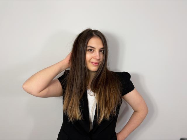 AnnaFlower69, com cabelos castanhos longos, blusa preta de manga curta, camisa branca, mão no cabelo, sorrindo, pele clara, em pé em frente a uma parede lisa, sem maquiagem, aparência natural, fofa..