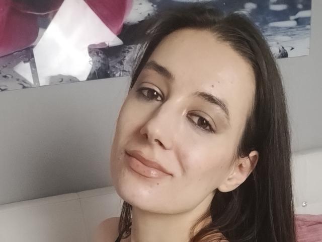 JuliaHuntis with shiny, slightly wet-looking face, brown eyes, and dark brown hair, smiling gently at the camera, showing her nose and lips. She has small, visible moles.