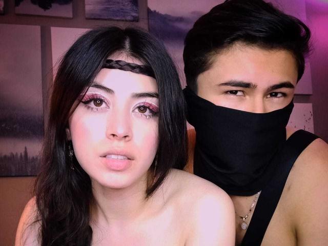 NoahAndRose with dark hair, braided headband, pink eyeliner, and bare shoulders, next to NoahAndRose with black mask, dark hair, and bare shoulders, in a dimly lit room.