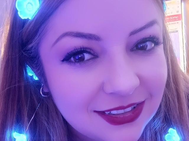 NatalyHami has blue-lit hair with flowers, dark red lipstick, and a cute smile. She's wearing a silver hoop earring, with eyelashes and a nose ring. Her tits are not visible.
