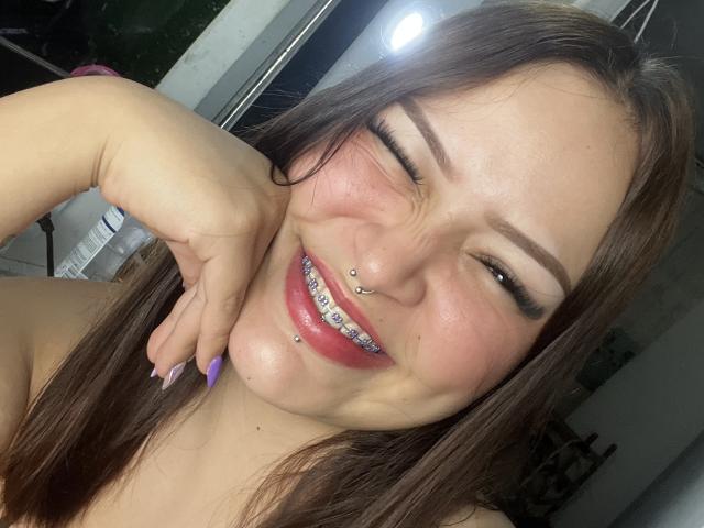 AllisonJustingb with a playful wink, smiling with pierced nose and lip, brown hair, purple nails, and a septum ring. She's got a cute, chubby-ass face and a sexy grin.
