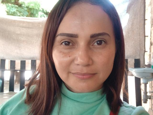 Sofia69s has medium brown skin, brown eyes, and straight brown hair. She's wearing a green turtleneck, smiling slightly, with a few small acne spots on her face.