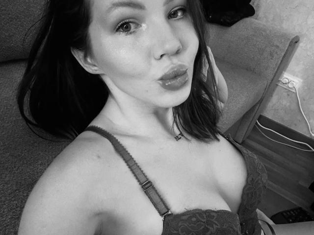 DeliciousChrissy with puffy lips, dark hair, and wearing a lace bra, showing her tits in a black-and-white selfie. Her nipples are slightly visible through the lace.