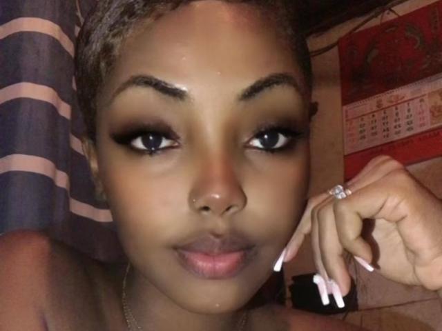 Moonisha, avec sa peau brun foncé, ses cheveux courts tressés, ses sourcils épais, son eye-liner noir et son rouge à lèvres rose, tient une bague à sa main droite, et on peut voir ses ongles longs et blancs..