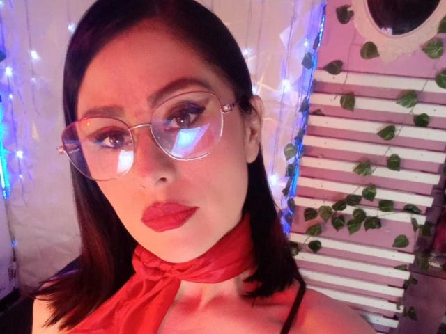 VioletaWhitee with red lipstick, glasses, and red scarf, showing off her tits in a selfie. She has dark hair and a cute, sexy look.