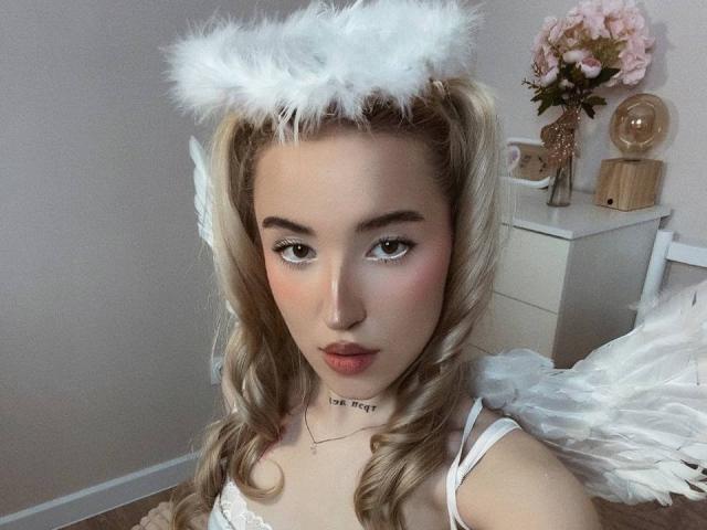 MillyPopa with blonde curls, wearing white angel wings, fluffy halo, and white lingerie, has a cute face, pink lips, and a necklace saying "love me."