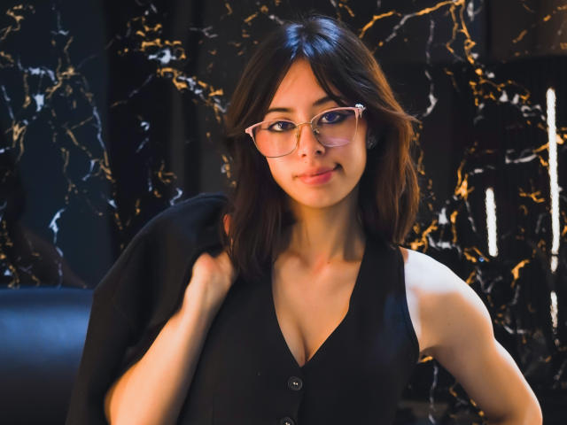 RoussMelix with glasses, black sleeveless top, buttoned down, showing her tits, dark wavy hair, slight smile, holding black garment, marble patterned background, soft light, confident look.