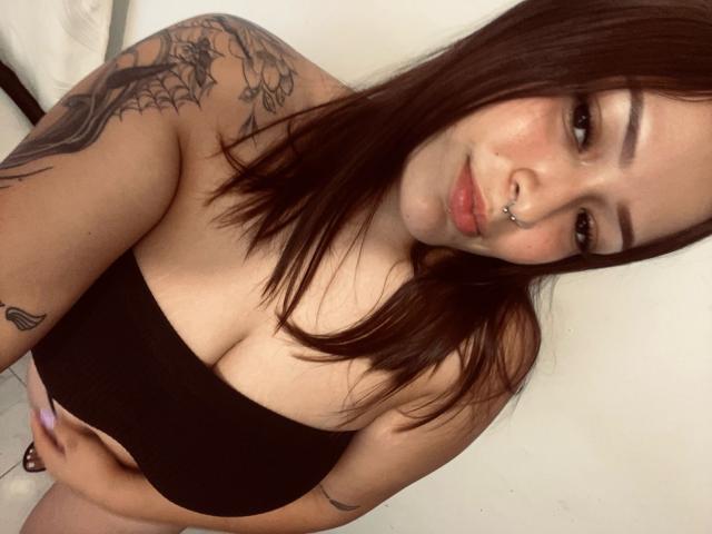 AlisonJustingb has brown hair, a nose ring, and tattoos on her shoulder. She's wearing a black tube top, showing her tits, and has a cute, sexy face.