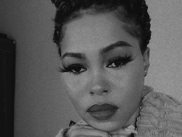 Sadeh69 has dark curly hair, thick eyebrows, long eyelashes, and full lips. She's looking at the camera with a serious expression, wearing a fuzzy top. Black and white.