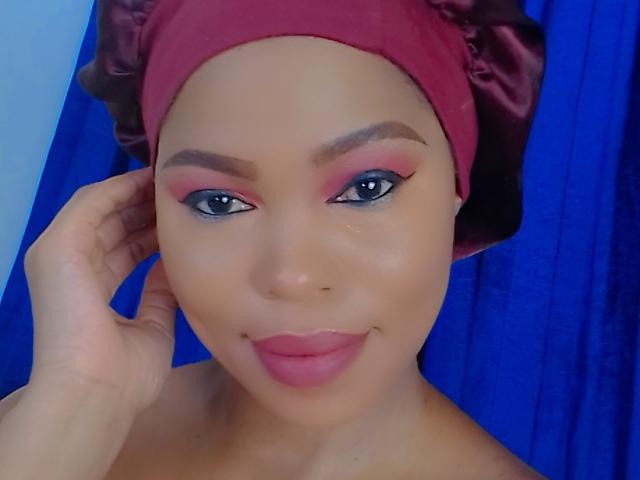 Sadeh69 has light brown skin, blue eyes, and pink lipstick. She's wearing a red headscarf, pink eyeshadow, and her hand is touching her head. Her tits are not visible.
