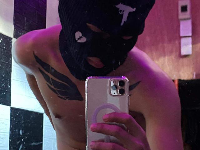 CockOfAsian, shirtless with black mask, tattoos on chest, holding phone, pink and purple lighting, mirror selfie, visible nipples, phone case with ring, mask has white skull design.