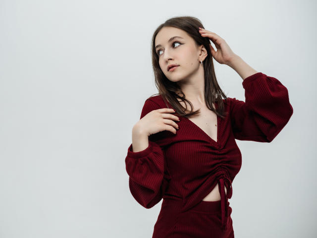 LilieFlower with brown hair, wearing a red ribbed crop top and matching pants, looking to the side, hand in hair, small tits, pale skin, white background.