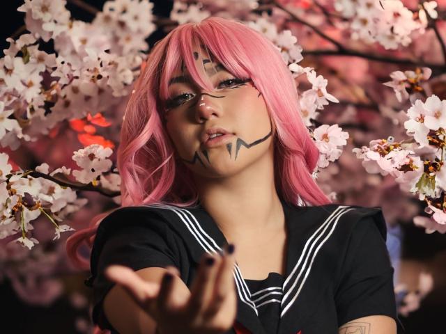 KelseyCoob with pink hair, glasses, black sailor top, face paint, reaching out, cherry blossoms in background, looking seductive, soft lighting, tattoos on arm, cute and sexy.