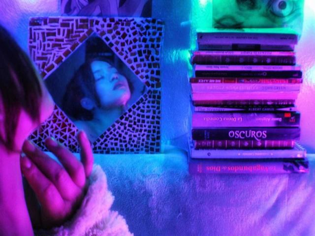LilithInTheEdenX's Hand mit zusammengelegten Fingern, neben einem mit Mosaik verzierten Foto eines Frauenansichts, gestapelte CDs mit violetten und blauen Neonlichtern..