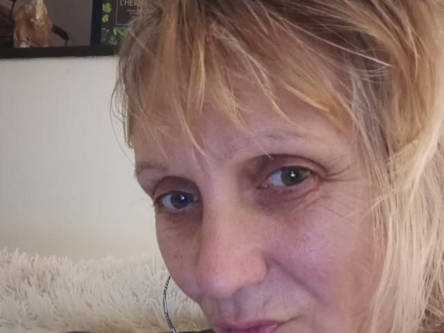 Suzanaa's face, showing blonde, messy hair, light skin, blue eyes, slight smile, and a small, subtle nose. She's looking directly at the camera. Her ass is not visible.