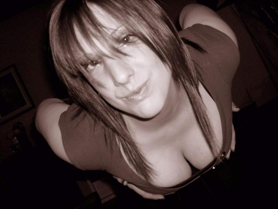 ValentinaNataliia69Hot with medium-length brown hair, looking down, smiling, wearing a low-cut top showing large, visible breasts, in a dimly lit, sepia-toned photograph.