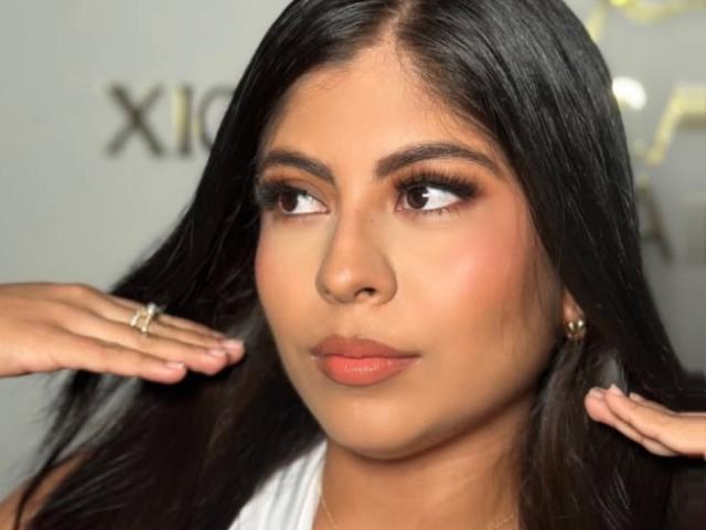 MelannieX69 with long black hair, brown eyes, and tan skin, looking to the side, hands near her face, wearing a white top, and a gold ring.