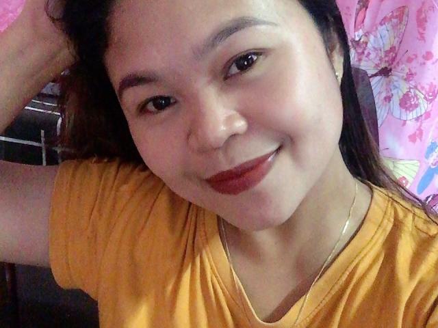 WildParadisePh has a cute smile, medium brown skin, and is wearing a yellow shirt. She has dark brown hair, red lipstick, and is touching her head with one hand.
