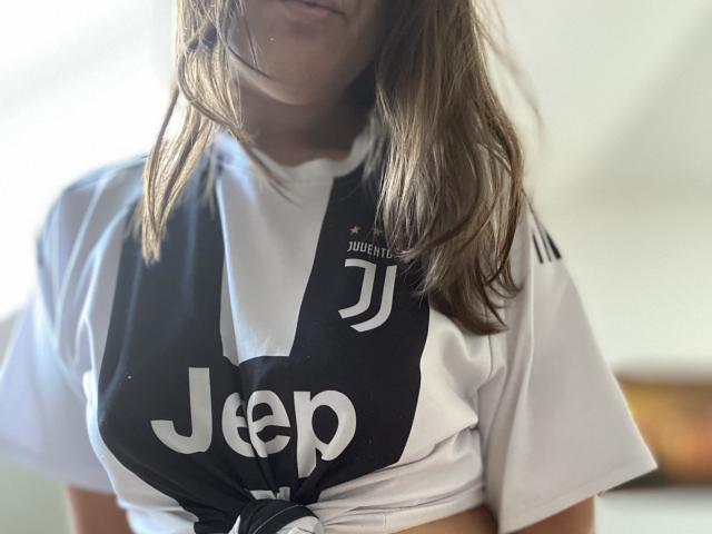 BrunettePrettie's tits are covered by a black and white Jeep sports vest, her long brown hair partially covering her face. Her white shirt is tied under the vest.