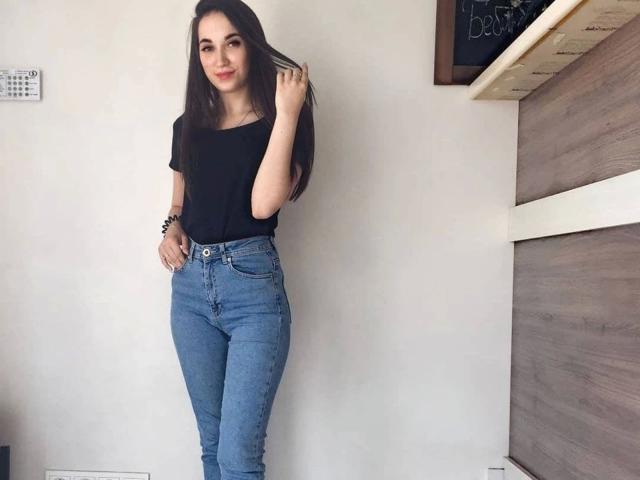 MissAnoliya-hot with long brown hair, black t-shirt, and blue high-waisted jeans, standing, hand in hair, smiling, slim, cute, small tits, no visible pussy or ass.
