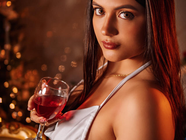 MiaLeiya with long red-brown hair, holding a glass of red wine, wearing a white halter top, looking at the camera, with soft, warm lighting, and a subtle smile.