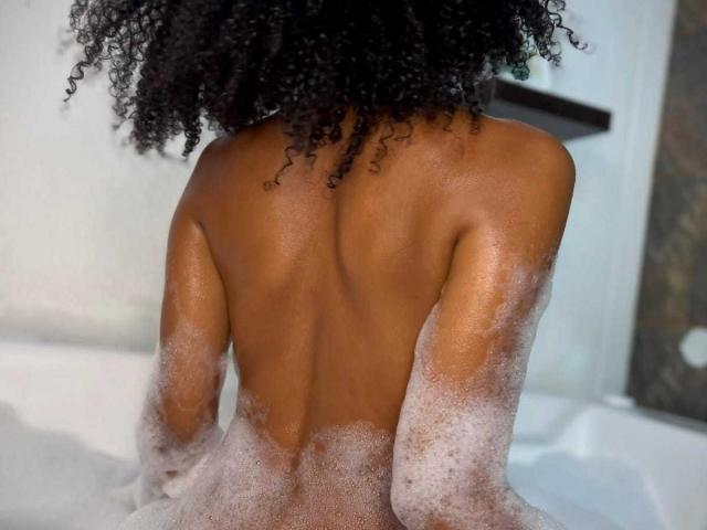 LizzyClasteton's back is to the camera, showing her wet, soapy skin and curly black hair. Her ass is partially covered in bubbles, sitting in a white tub.
