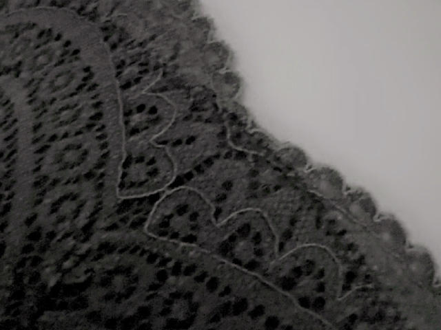 A grey, lace-like fabric with intricate patterns, featuring heart and circular motifs, is shown in a close-up. Boobs-like texture, detailed with small holes and raised edges.