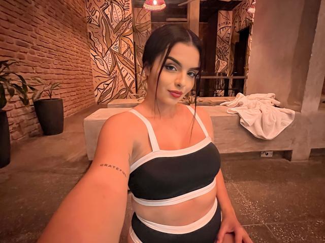 NovaDixon with black and white sports bra, showing her tits and a tattoo on her right arm, taking a selfie in a dimly lit room.
