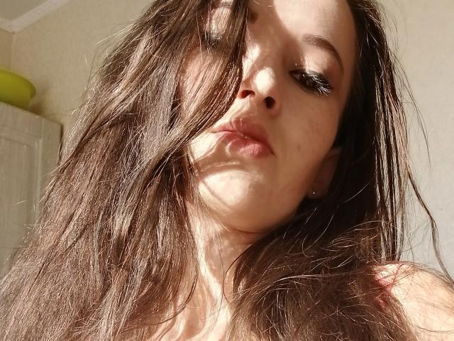 LuxCrow, met lang, rommelig bruin haar, een door de zon verlicht gezicht en lichtjes opgetrokken lippen, met ogen half gesloten, waarbij een schaduw haar rechterwang bedekt, in zacht, natuurlijk licht..