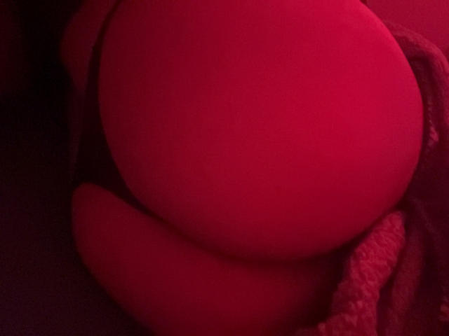 Red-lit photo of BubblyBabe's round, bare ass in black underwear, with a textured fabric partially covering the right side. BubblyBabe's skin is smooth and slightly shiny.