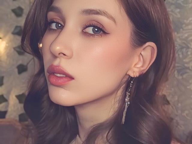 ShawtyVi has pretty brown eyes, pink lipstick, and wavy brown hair with a small nose stud and long, dangling earrings. Her skin is smooth and slightly flushed.