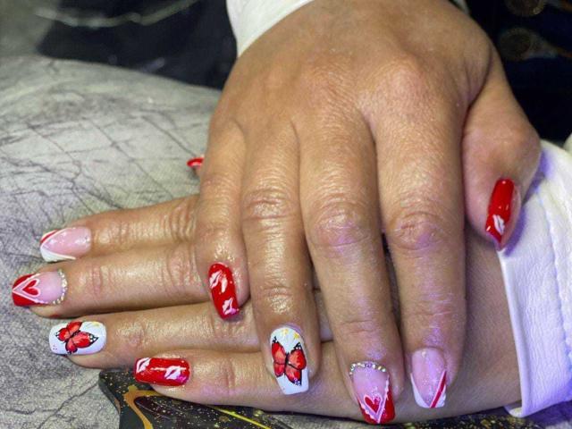 KinkyVane's hands, showcasing bright red and white nail art with red butterflies, red hearts, and white tips, resting on a patterned surface. Boobs are not visible.