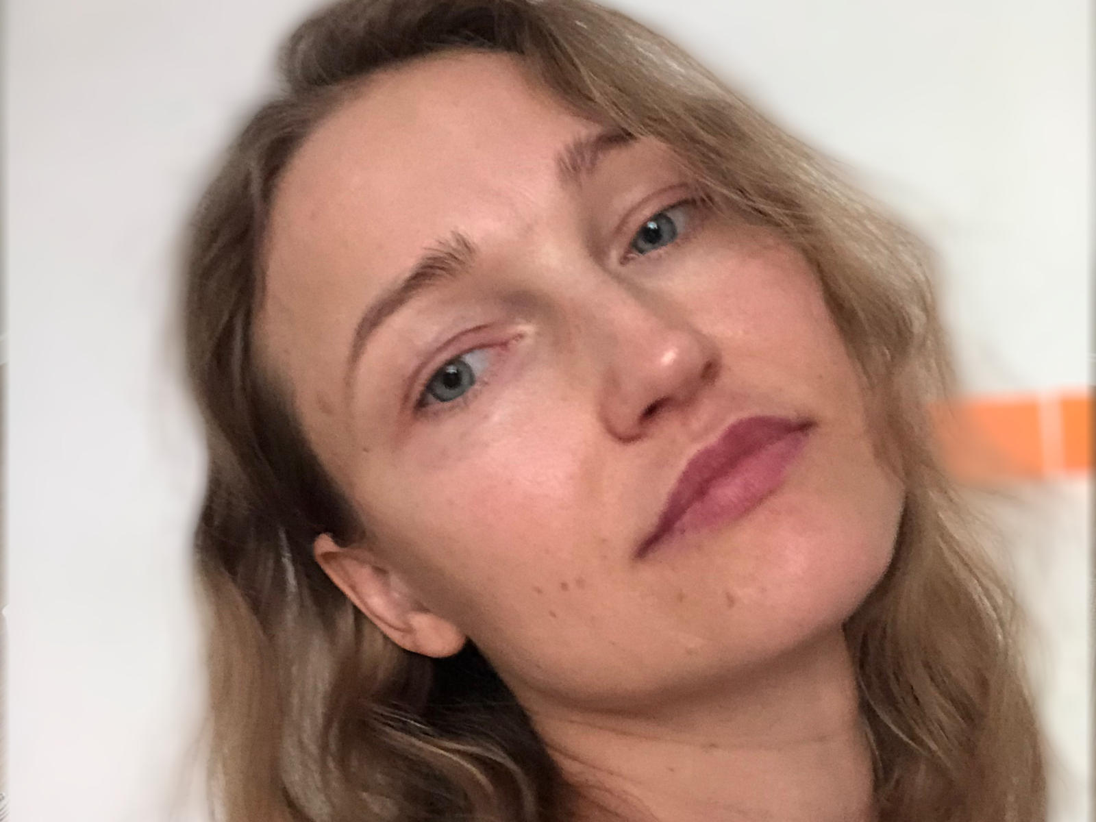 IremElmah ha la testa leggermente inclinata, capelli castano chiaro ondulati, occhi verdi e rossetto rosa. Il suo viso è chiaro con piccole lentiggini. La foto è un selfie..