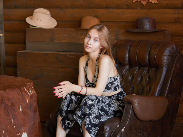 EmiliaMarshall with long blonde hair, small tits, wearing a black floral halter dress, sitting on a brown leather chair, hands with red nails, wooden wall, hats behind her.