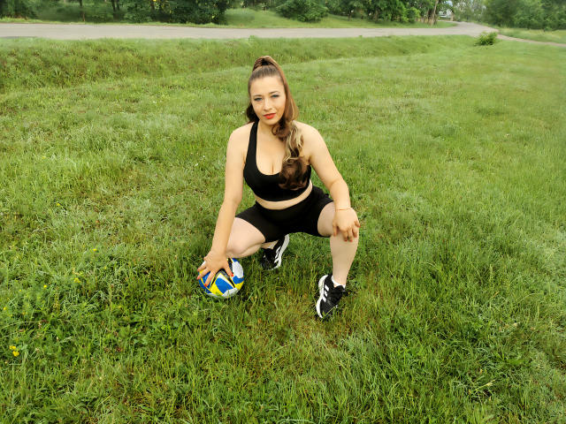EmmaSeduction, squatting on grass, wearing black sports bra and shorts, holding soccer ball, with her tits slightly visible, in black and white sneakers, with her hair in a ponytail.