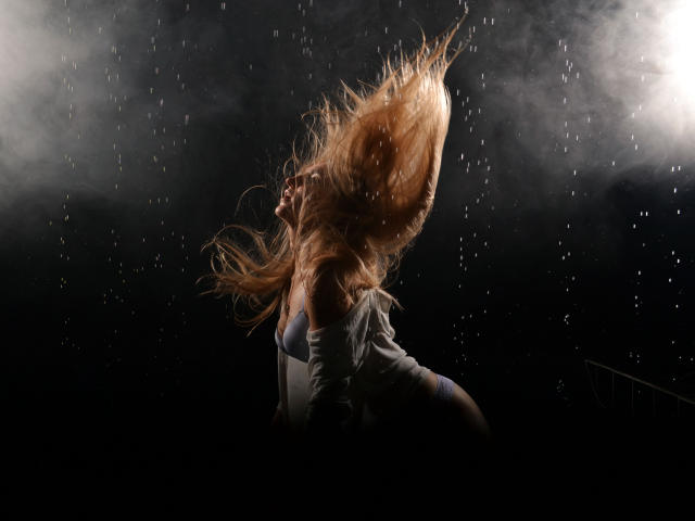 NadinTurner's blonde hair flies up wildly as raindrops hit her. She's in a white off-shoulder top, with water droplets visible in the dark, moody shot.