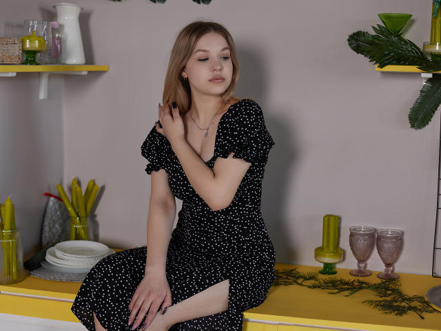 SimonaForman with small tits, wearing a black polka dot dress, sitting on a yellow countertop, touching her chest, eyes closed, light brown hair, subtle makeup, relaxed expression.