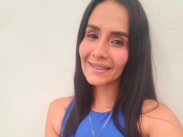 AnnaRous a de longs cheveux noirs, des yeux marrons et un petit sourire. Elle porte un haut bleu sans manches avec un collier en argent. Ses seins sont petits et elle est mignonne..