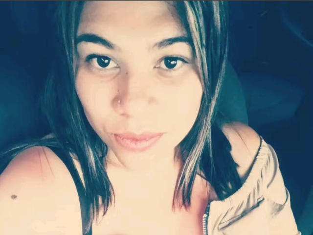 AlmaWhite69 with light skin, brown eyes, and straight brown hair, wearing a beige jacket, showing a small mole on her left shoulder, and slightly pouted lips.