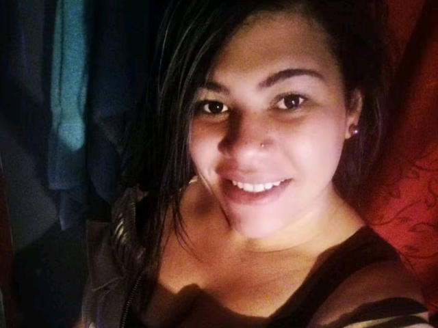 AlmaWhite69 with medium brown skin, dark straight hair, small nose ring, smiling, showing white teeth, wearing a brown top, earrings, and looking at the camera.