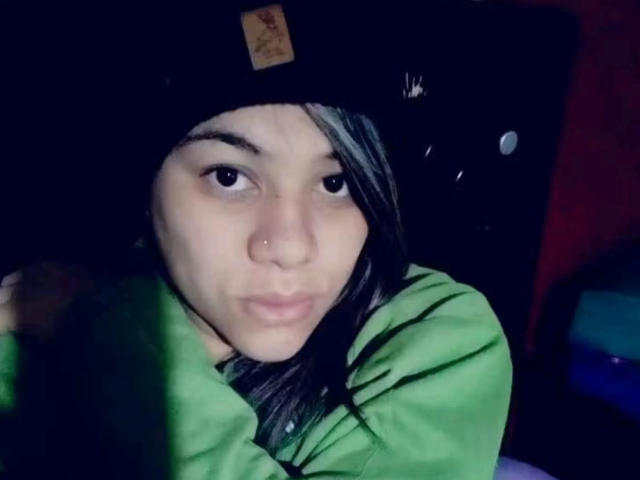 AlmaWhite69 has a pensive expression, wearing a black beanie and green hoodie, with long dark hair and a nose piercing, looking slightly to the side.