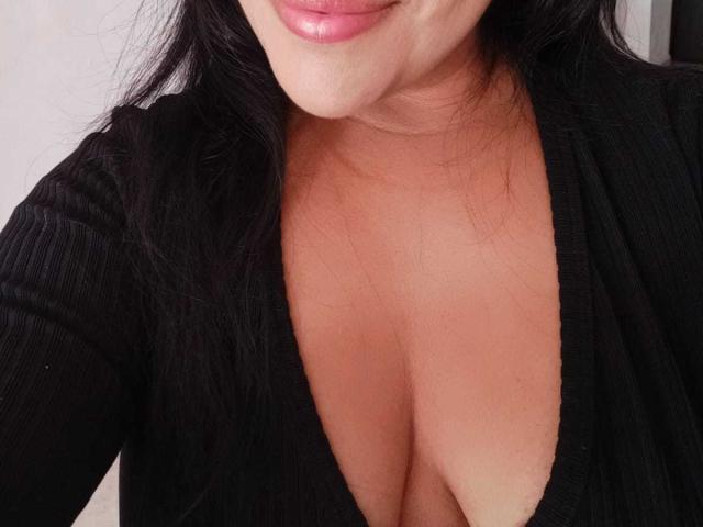 PaulinaQueens' black V-neck top, showing her tan skin and cleavage, with her pink lips slightly smiling, and long black hair falling around her shoulders.