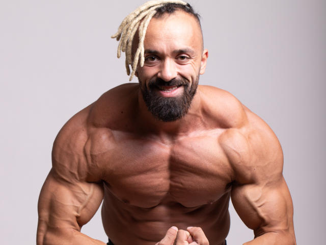 Alexhunk69 is a muscular, shirtless dude with blonde dreadlocks, a black beard, and a happy smile. His big, bulging biceps and defined abs are totally impressive.