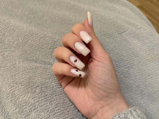 SugarrX's hand with long, white, almond-shaped nails, each nail featuring a small red dot, resting on a gray textured towel.