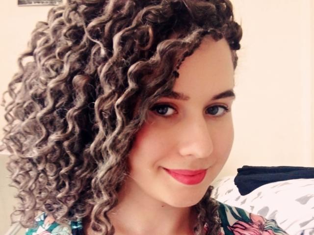 MarlanViviane has curly brown hair, blue eyes, red lipstick, and a cute smile. She's wearing a colorful patterned top. Her ass is not visible in this shot.