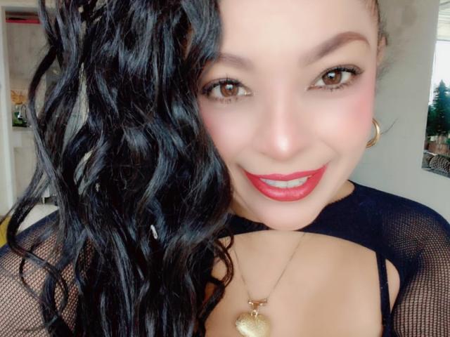 KarenCurlyHair has wavy black hair, brown eyes, red lipstick, and wears a black mesh top with a gold necklace. Her tits are slightly visible through the top.
