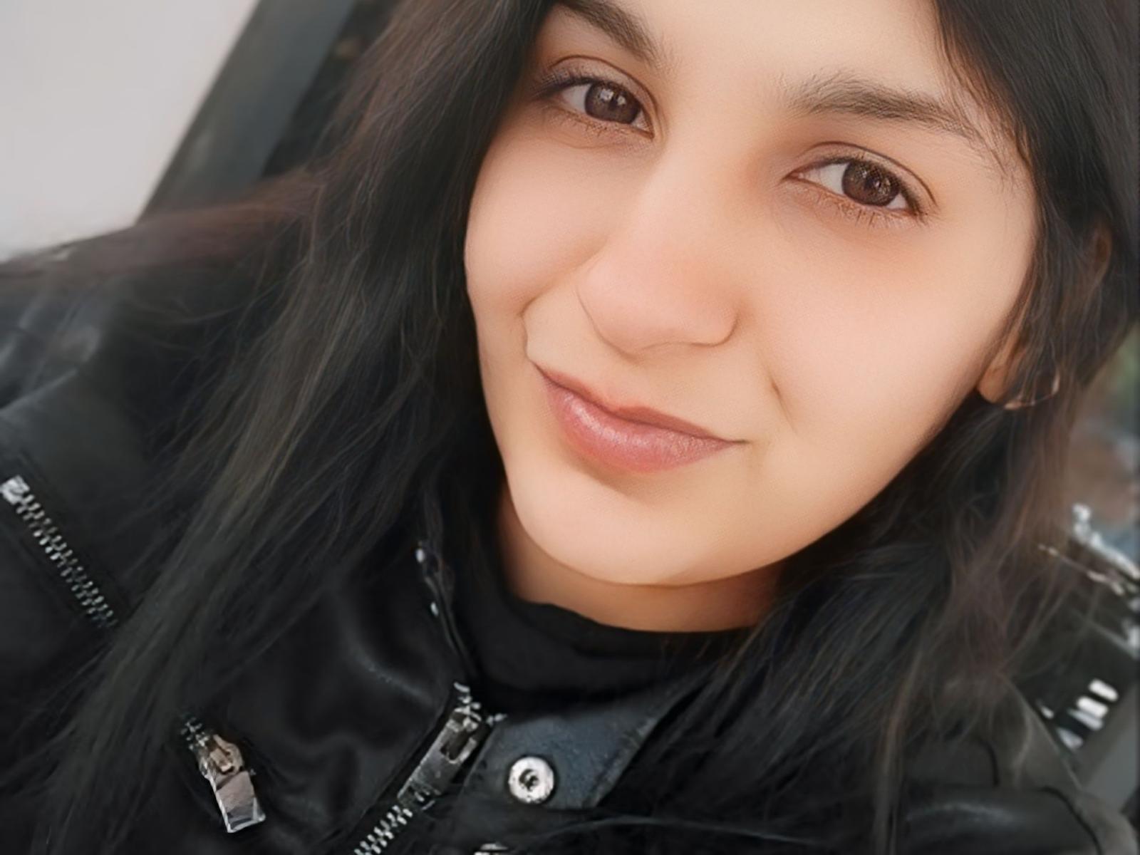 KettyPretty has a cute face, brown eyes, and black wavy hair. She's wearing a black leather jacket with zippers, and she's smiling softly. Her nose is slightly upturned.