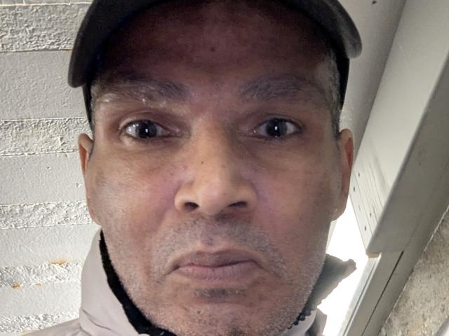 A flat, minimalist style image with a large, central, slightly faded red and white shield-like symbol. The shield has a simple, bold design with no additional elements.